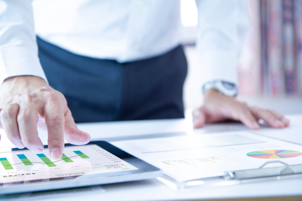 Business man touching a tablet touch screen analysing on business performance reports and returning on investment, ROI, or investment risk analysis.